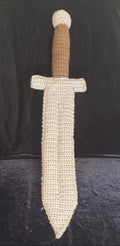 A crocheted toy or decorative sword with a textured gray blade and guard, and a brown handle, displayed against a black fabric background.