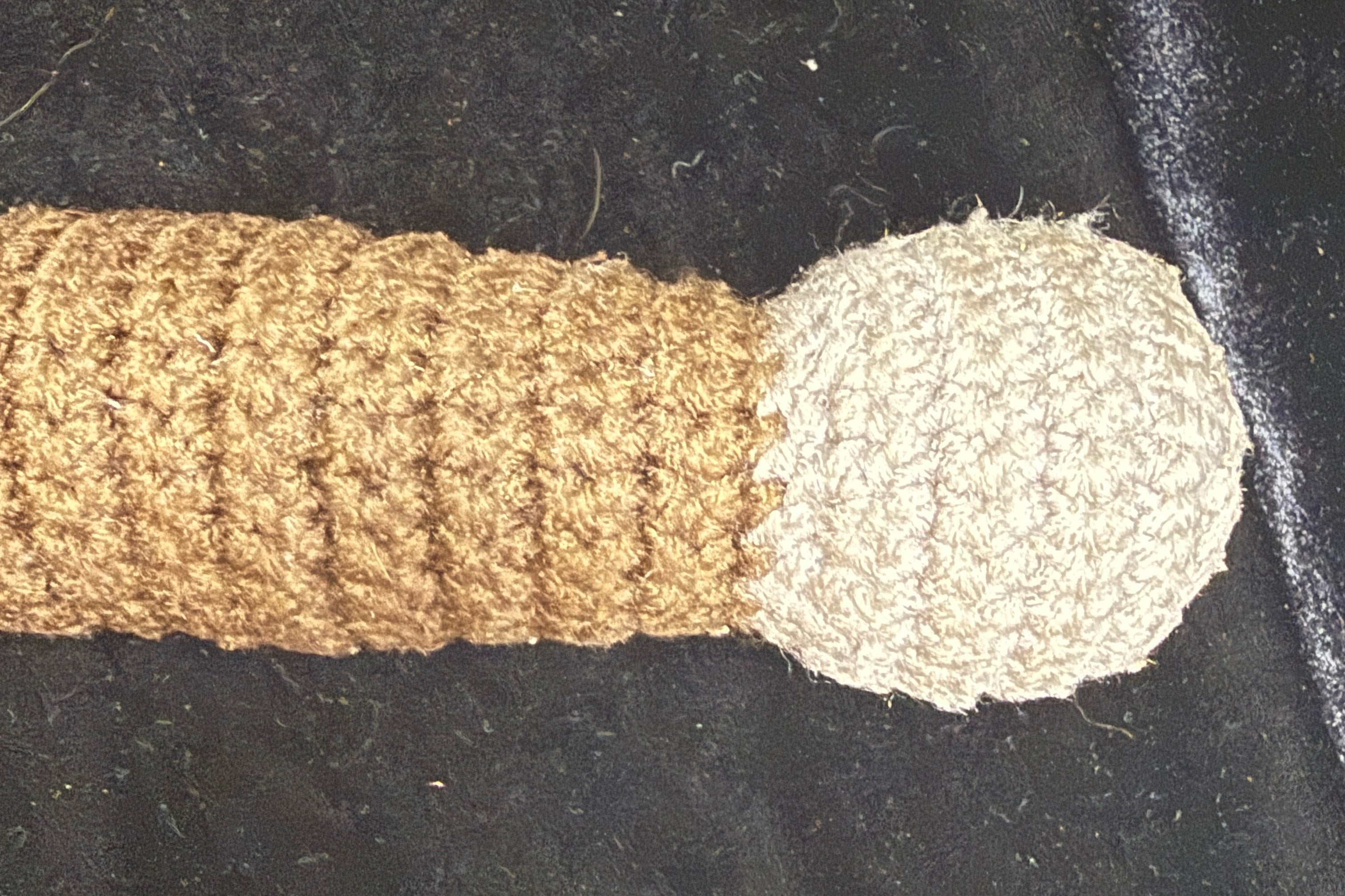 Crocheted dagger brown handle and gray pommel on a black bakground